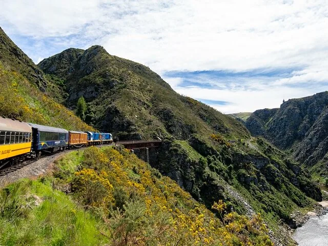 Taieri Gorge Railway train traveling through rugged mountain landscape with river below