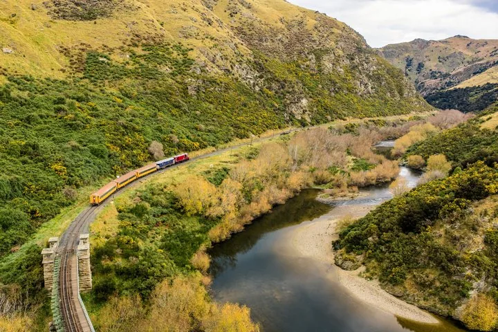 Train traveling alongside a winding river in a scenic green valley