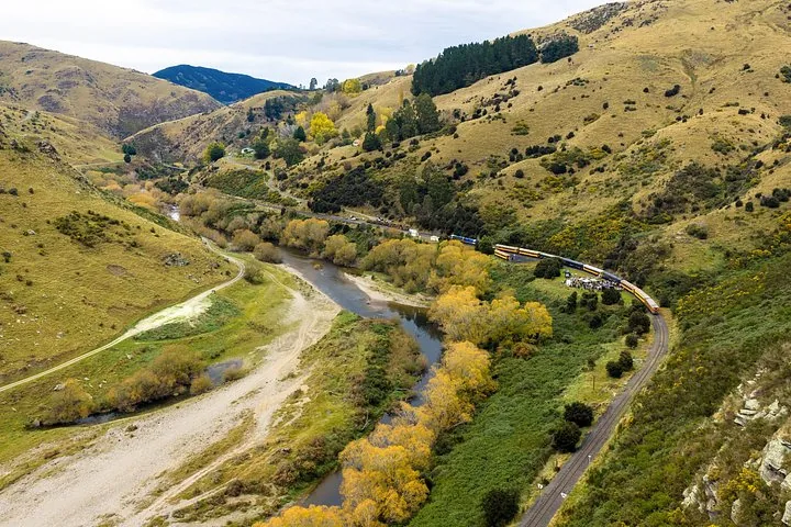Aerial view of a train traveling through a river valley with yellow trees