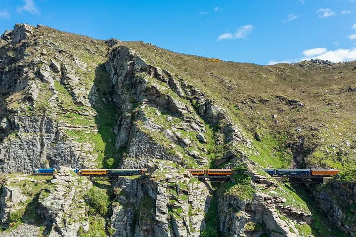 Train passing over a bridge built into a steep, rocky cliff face