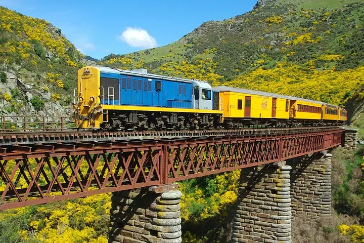 Blue and yellow locomotive leading a passenger train across a rusty bridge